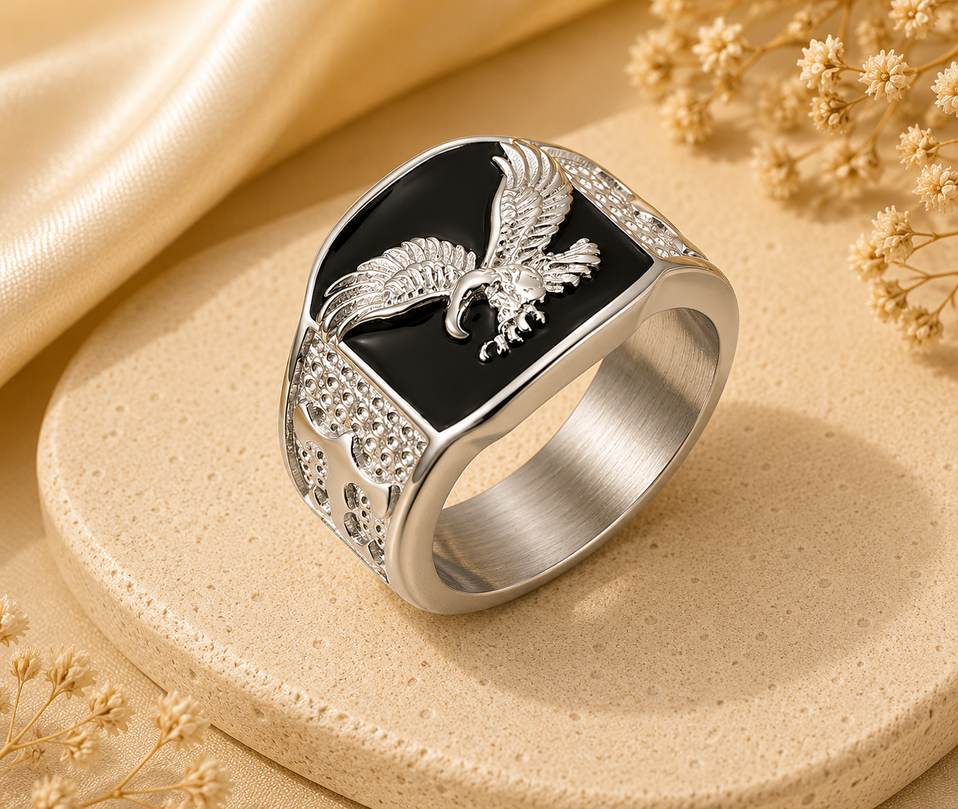 Silver ring with an eagle design on a beige surface with dried flowers.