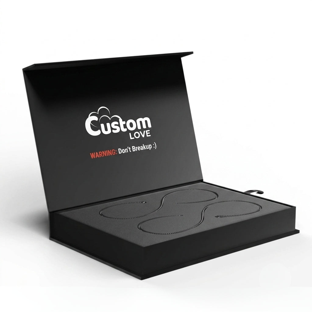 An open black presentation box on a white background, with the inside lid printed with the words 'Custom LOVE' and a small red warning note. The box contains a black item with an irregular wavy outline molded into the base.
