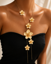 Gold floral necklace on a person wearing a black top against a neutral background