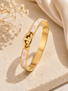 Gold bracelet with a heart design on a beige surface with dried flowers