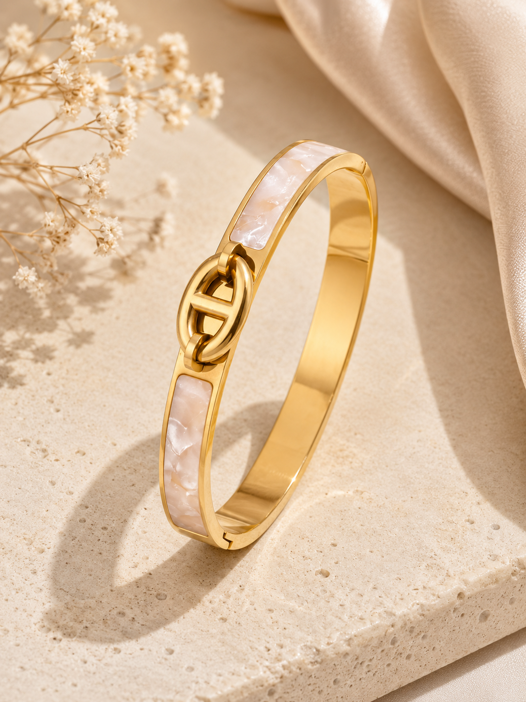 Gold bracelet with a heart design on a beige surface with dried flowers