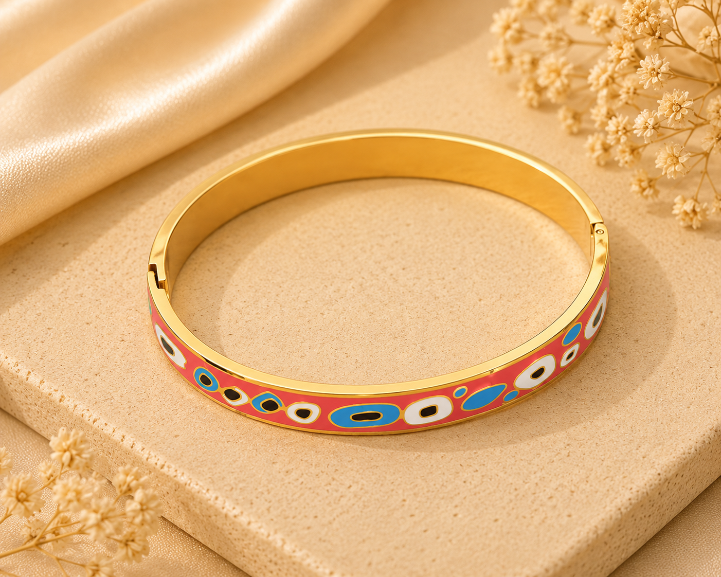 Gold bangle with colorful pattern on a beige surface with dried flowers