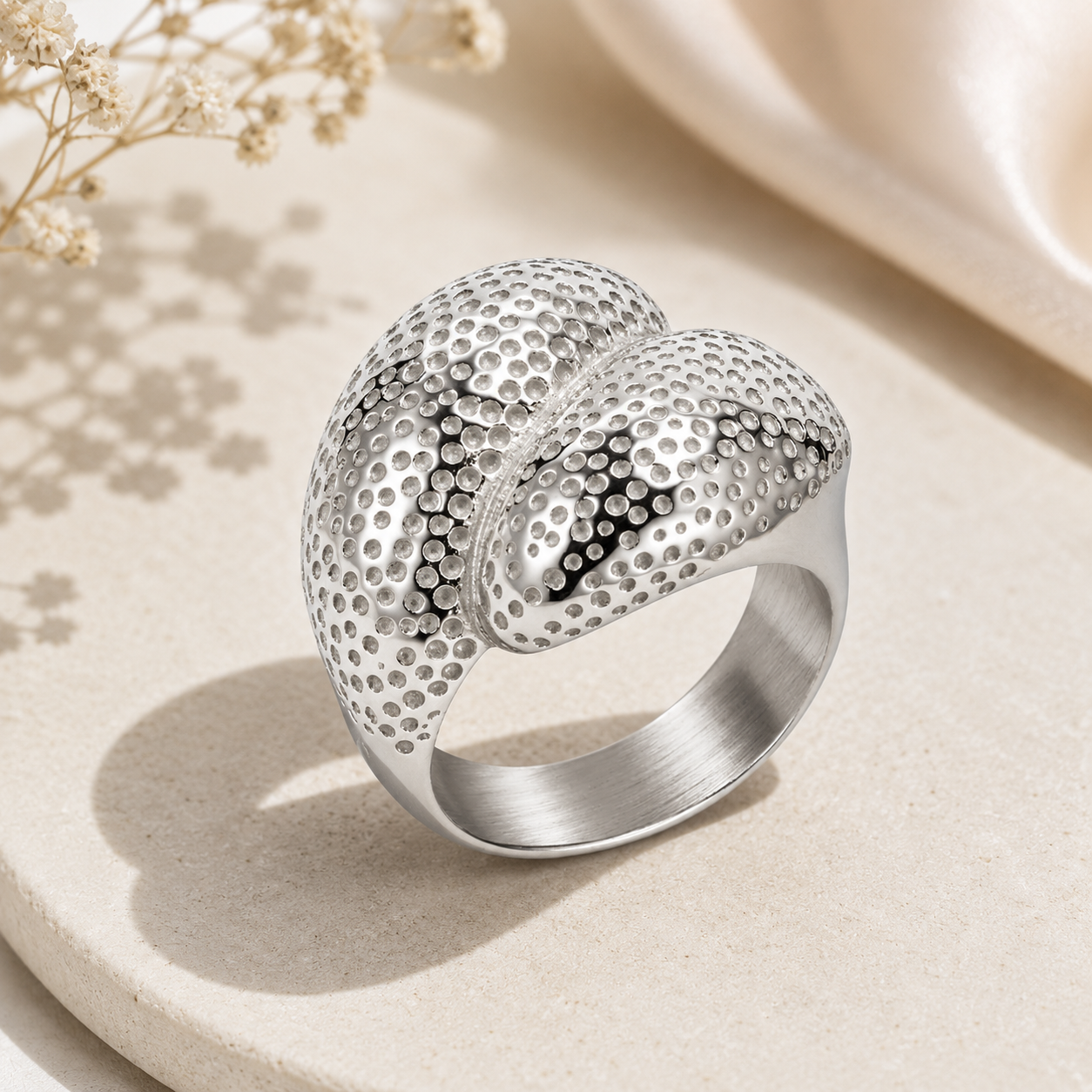Silver textured ring on a light beige surface with dried flowers.