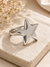 Silver star-shaped ring with 'Blessing' engraving on a beige stone surface.