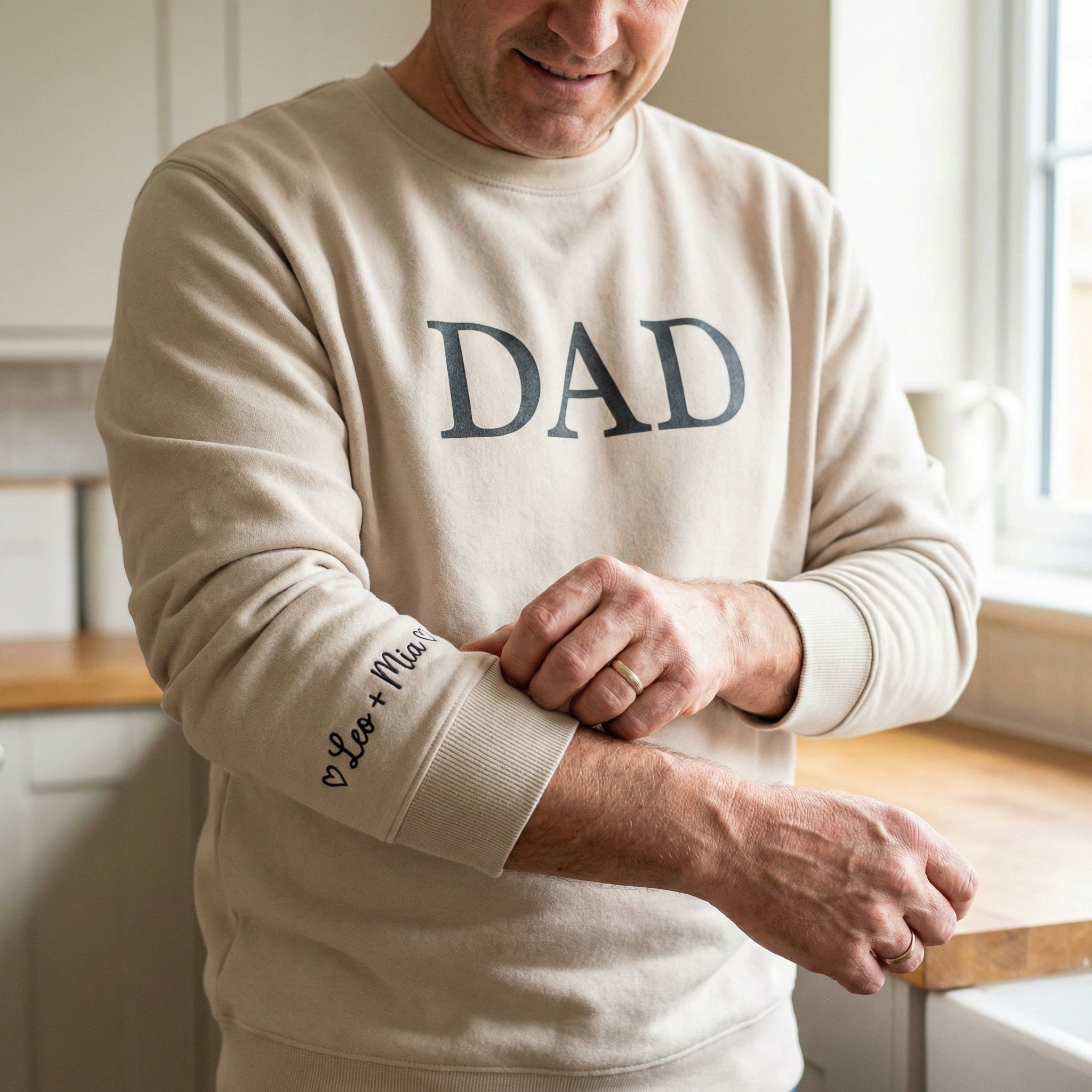 Man wearing a beige sweatshirt with 'DAD' printed on it, standing in a kitchen.