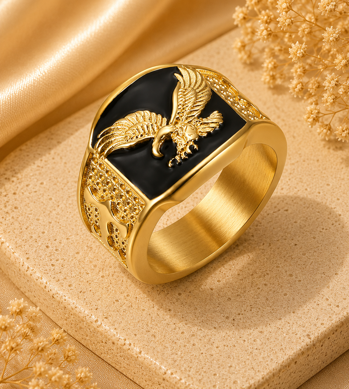 Gold ring with an eagle emblem on a beige surface with dried flowers.